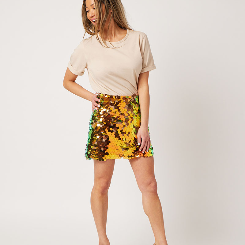 Woman wearing the Perfect Rolled Sleeve T-Shirt in Latte and a gold sequin skirt and nude pumps looking to the side with hand on hip