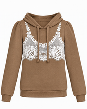 A tan long-sleeve hoodie featuring a white lace bralette embroidered across the chest