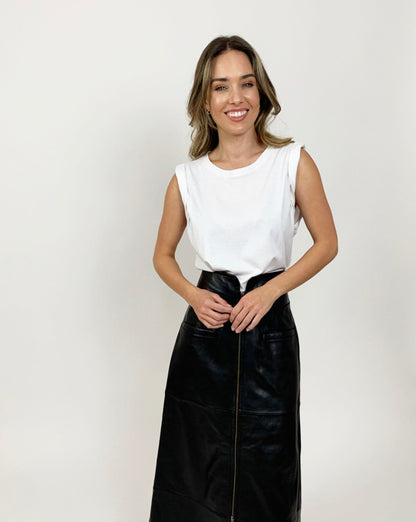Thin, white model with brunette hair smiling while wearing white pima cotton muscle tee and long black leather skirt holding her hands in front