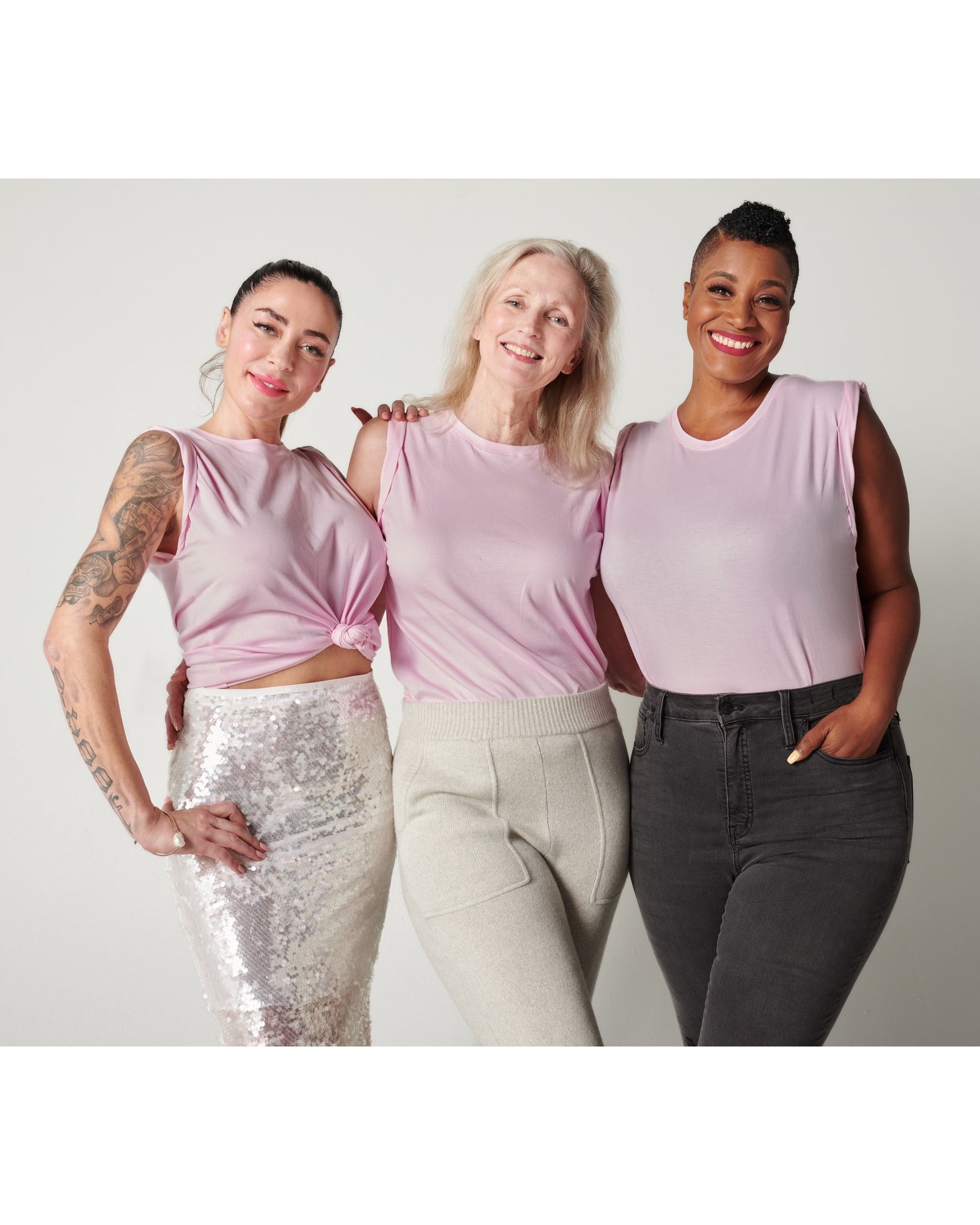 3 fuller bust models hugging and smiling while wearing Pink pima cotton muscle tee in silver sparkle skirt, cream joggers and black jeans