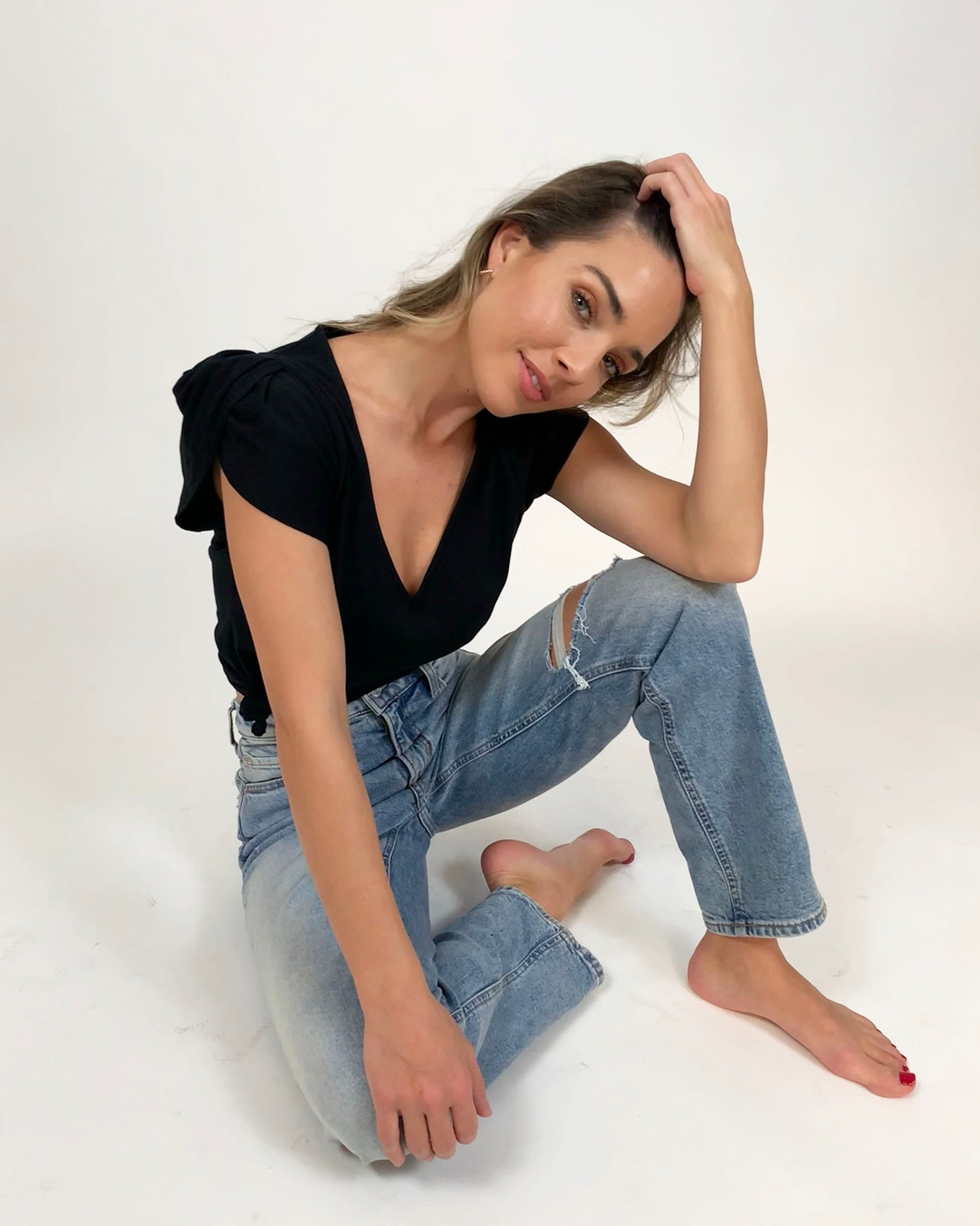 Black supima cotton v-neck, tulip sleeve tee on model sitting down in jeans