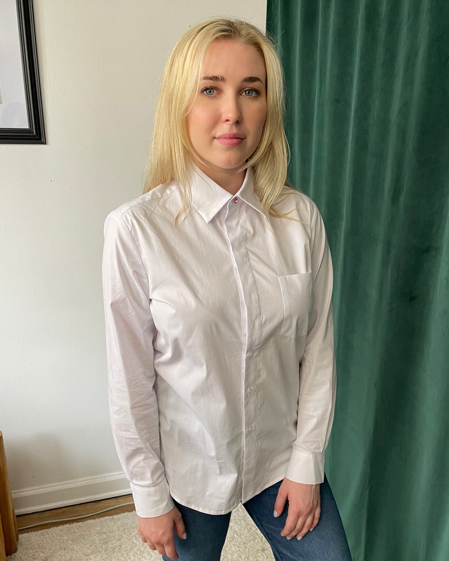 White organic cotton long sleeve button down fully buttoned with pink cuff link on blonde white model wearing blue jeans in front of green curtains