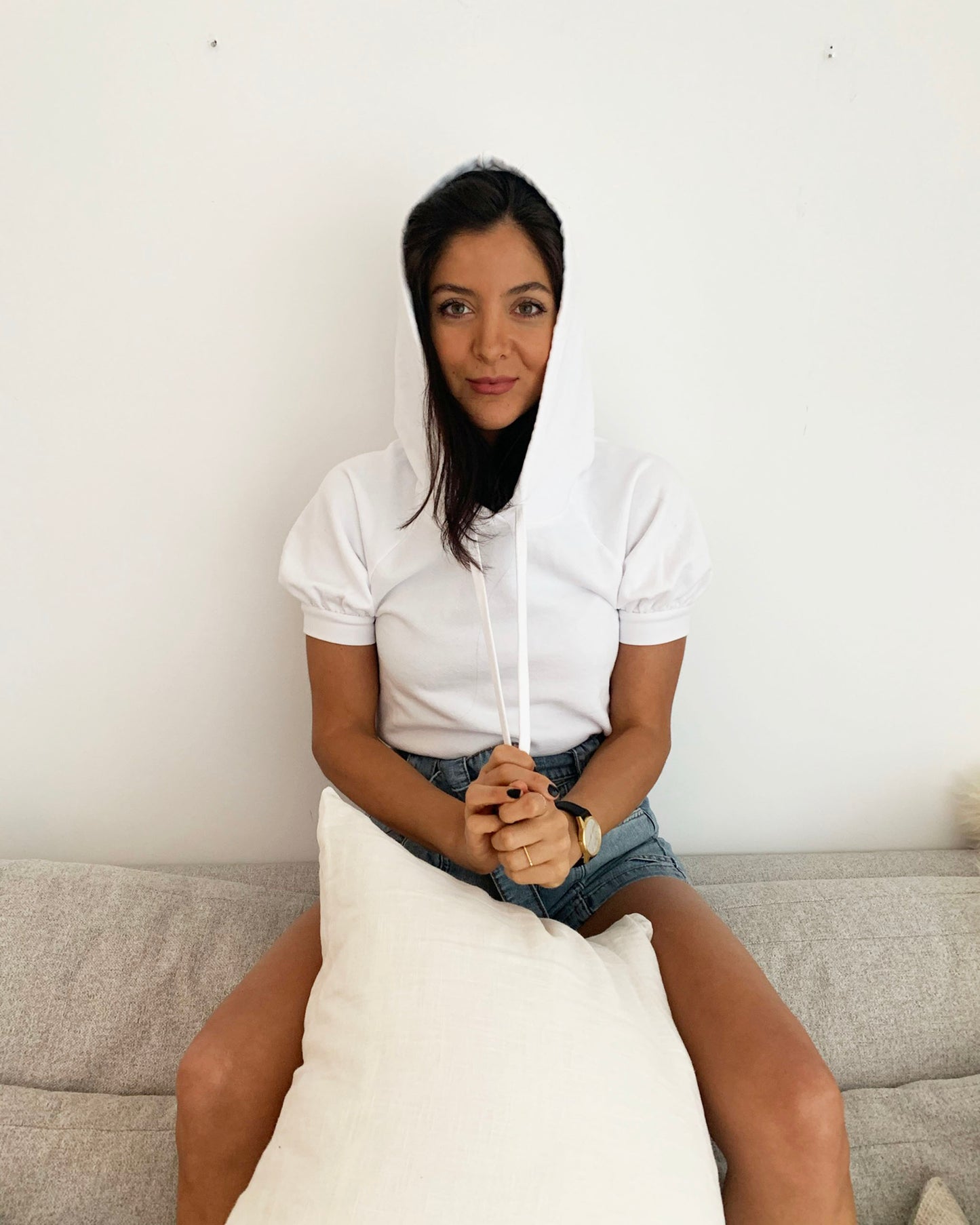 White organic cotton short sleeve sweatshirt on model sitting on grey couch, holding drawstrings with white pillow in between legs