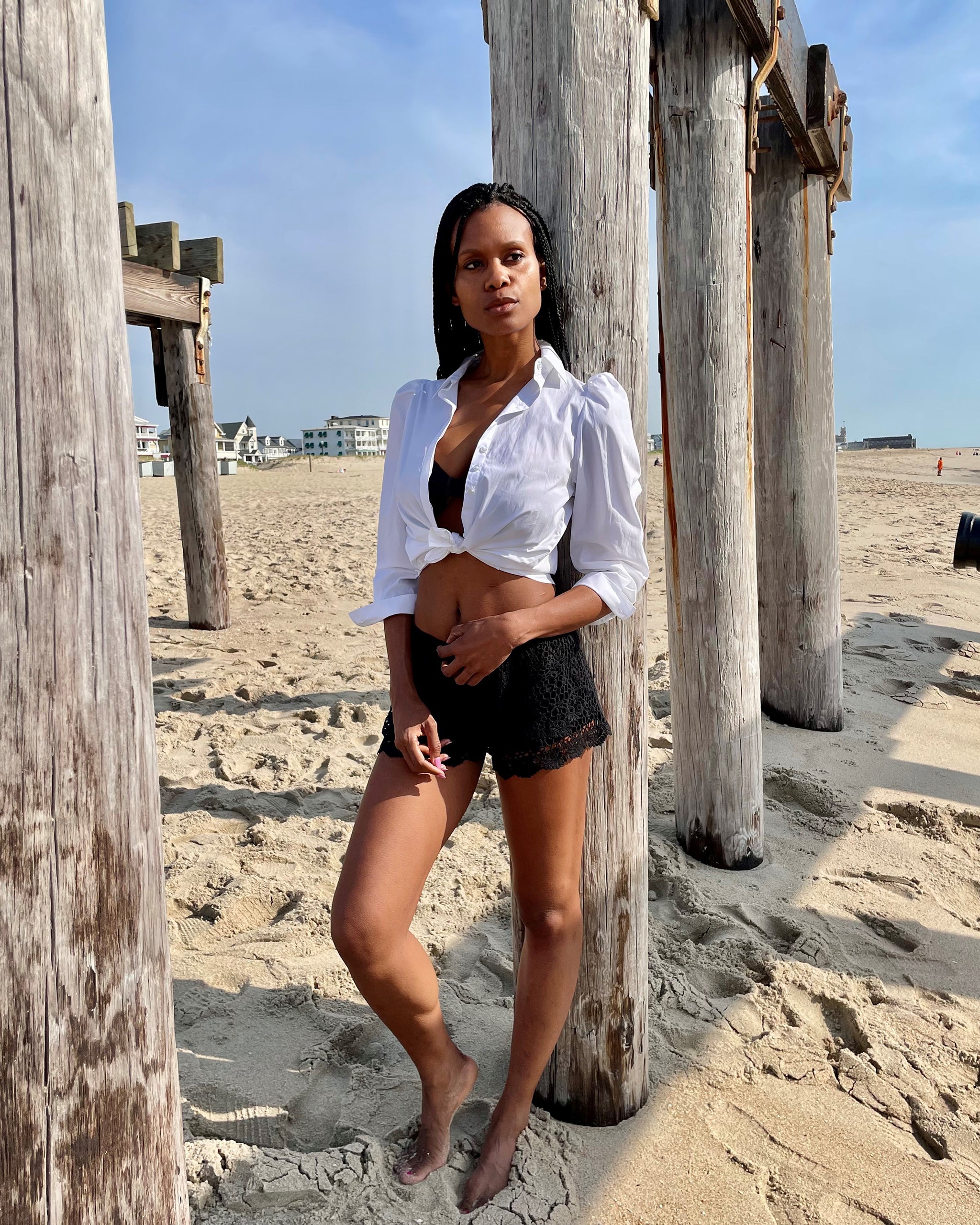 White cotton puff sleeve button down in front tie on model wearing black shorts and black bra on beach