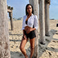 White cotton puff sleeve button down in front tie on model wearing black shorts and black bra on beach