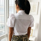 Back detail of white cotton short sleeve button down on model wearing leopard shorts looking out window