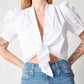 Detail of white cotton puff sleeve wrap top on model wearing blue jeans with hands on hips