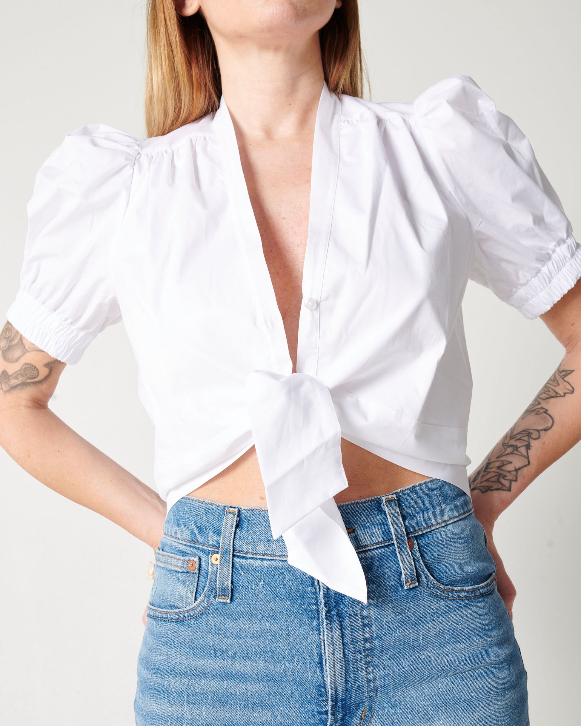 Detail of white cotton puff sleeve wrap top on model wearing blue jeans with hands on hips