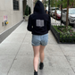 Back detail of black cotton fleece puff sleeve sweatshirt on model wearing blue shorts walking on street