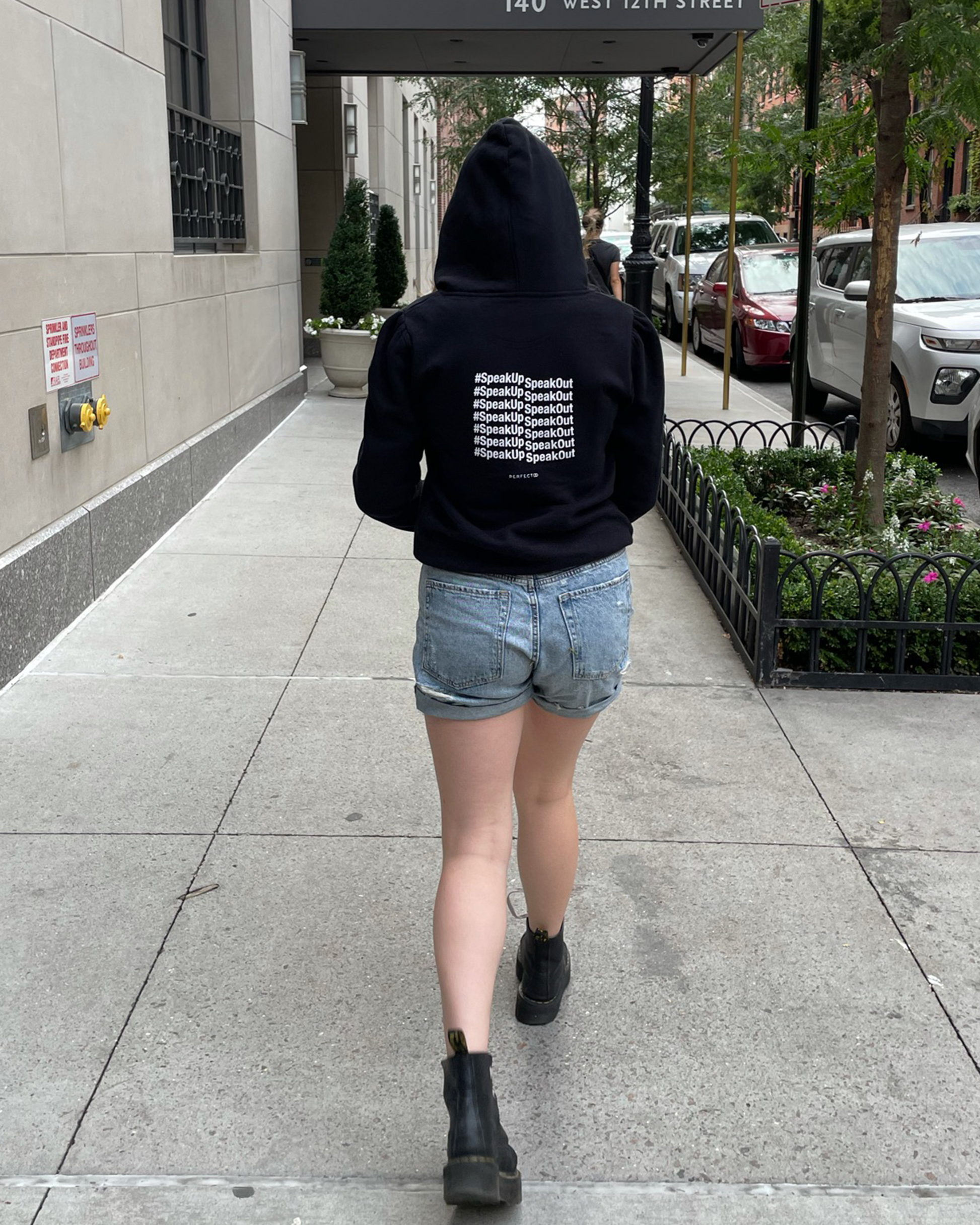 Back detail of black cotton fleece puff sleeve sweatshirt on model wearing blue shorts walking on street