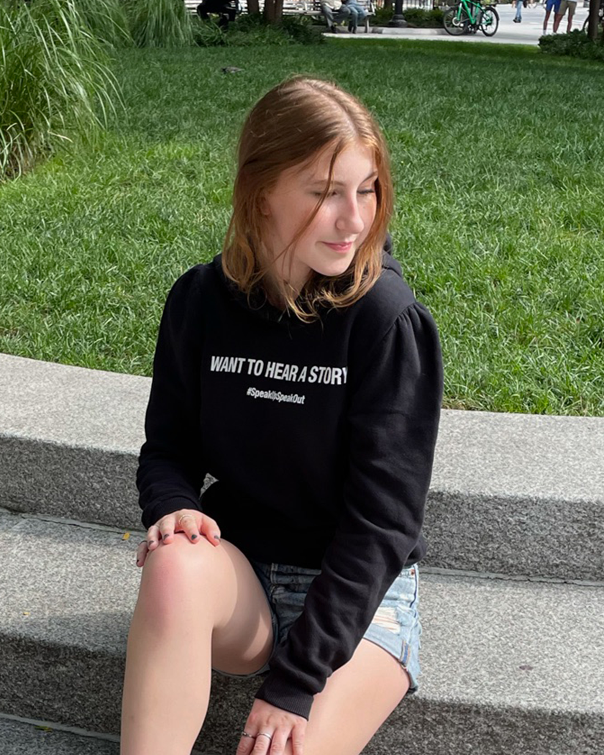 Side profile of black cotton fleece puff sleeve sweatshirt on model sitting on park steps