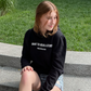 Side profile of black cotton fleece puff sleeve sweatshirt on model sitting on park steps