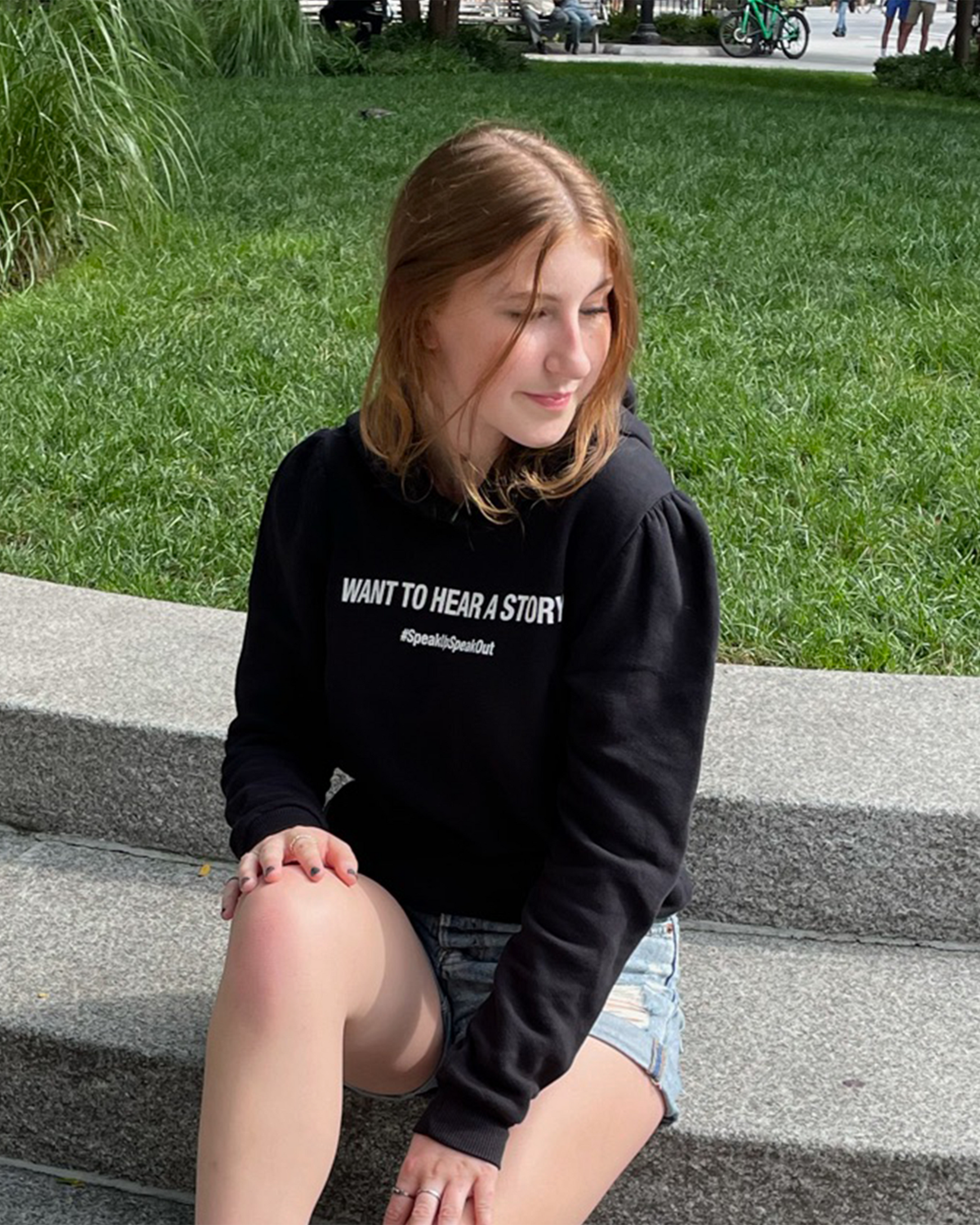 Side profile of black cotton fleece puff sleeve sweatshirt on model sitting on park steps