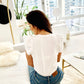 Back of White supima cotton scoopneck tulip sleeve tee on brunette model sitting on couch in NYC apartment