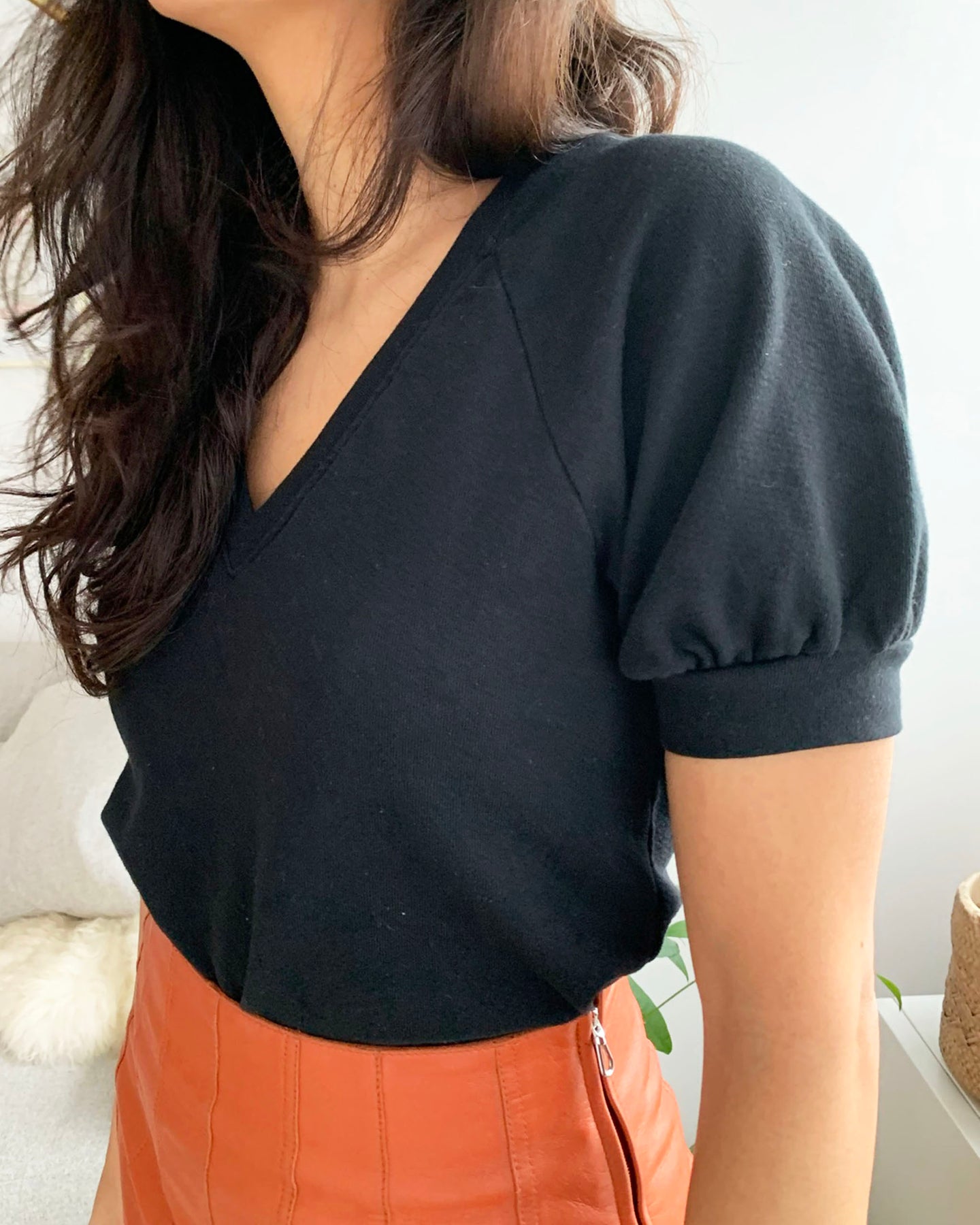 Side profile of sleeve detail of black organic cotton v-neck sweatshirt on model in orange skirt