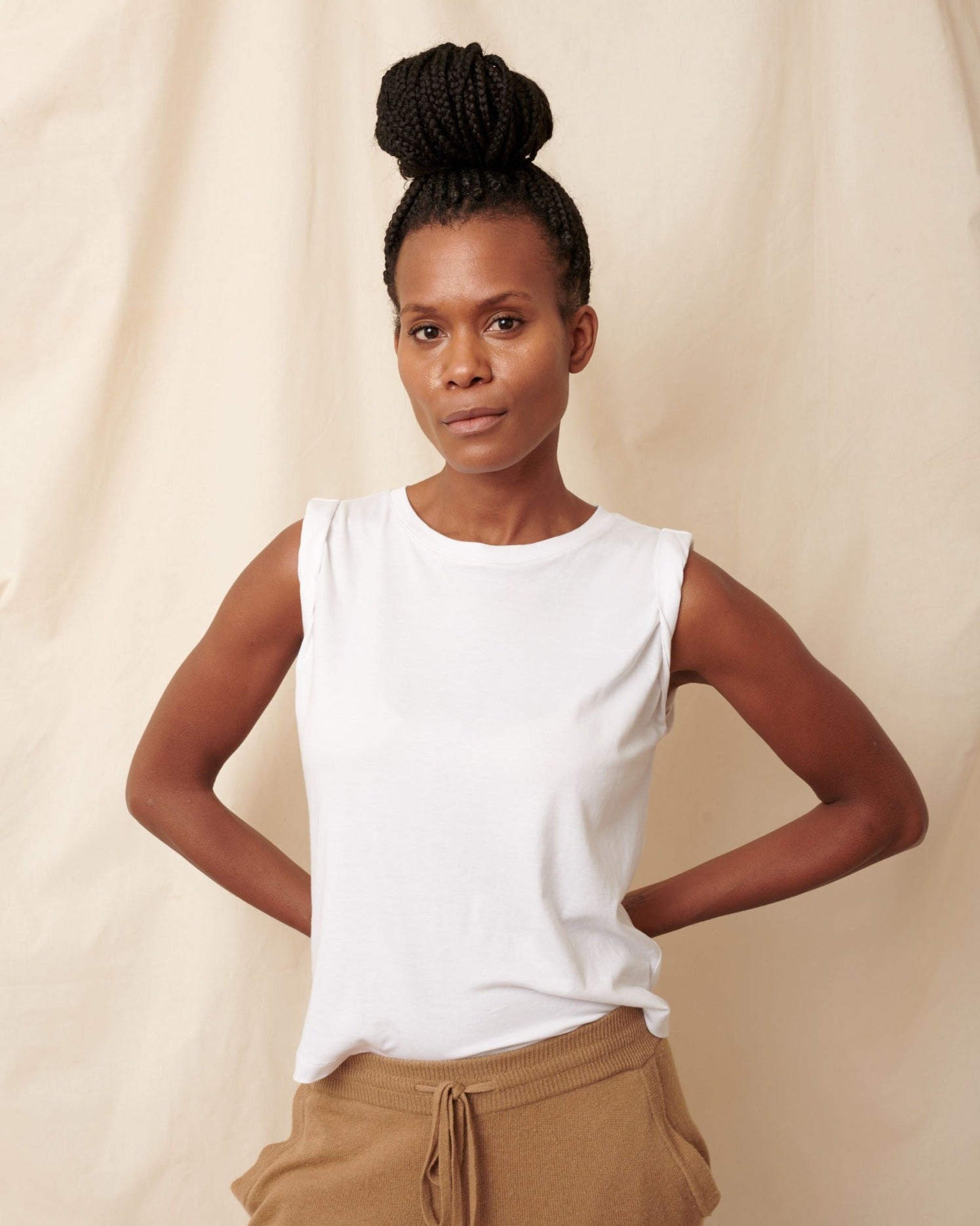 Thin, large chested black model wearing white pima cotton muscle tee with hands behind her back 