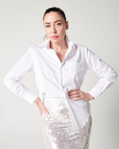 White organic cotton long sleeve button down french tucked into silver sparkle skirt on white model with hands on hips