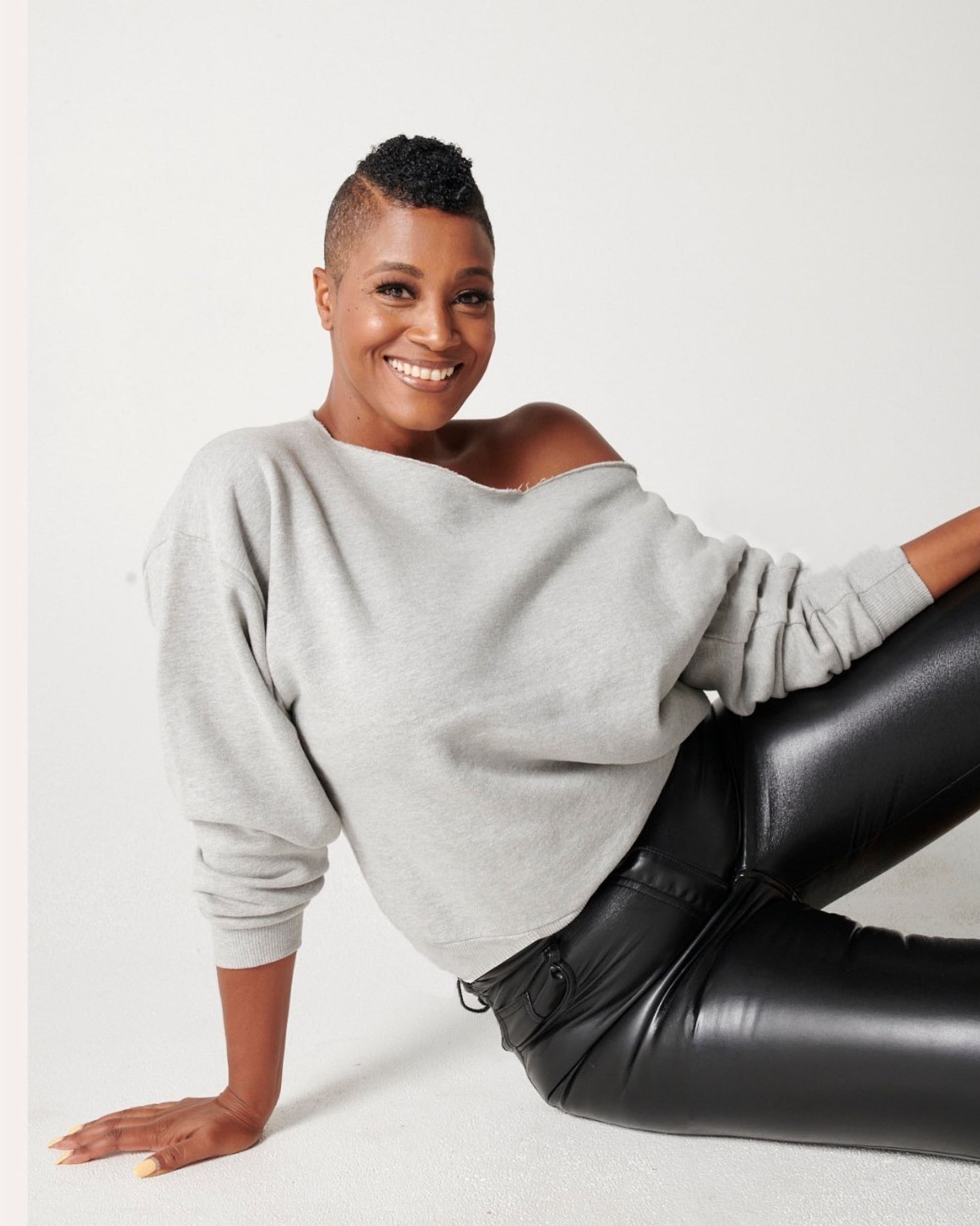 Heather grey cotton fleece off-the-shoulder sweatshirt on model sitting down in black leather pants