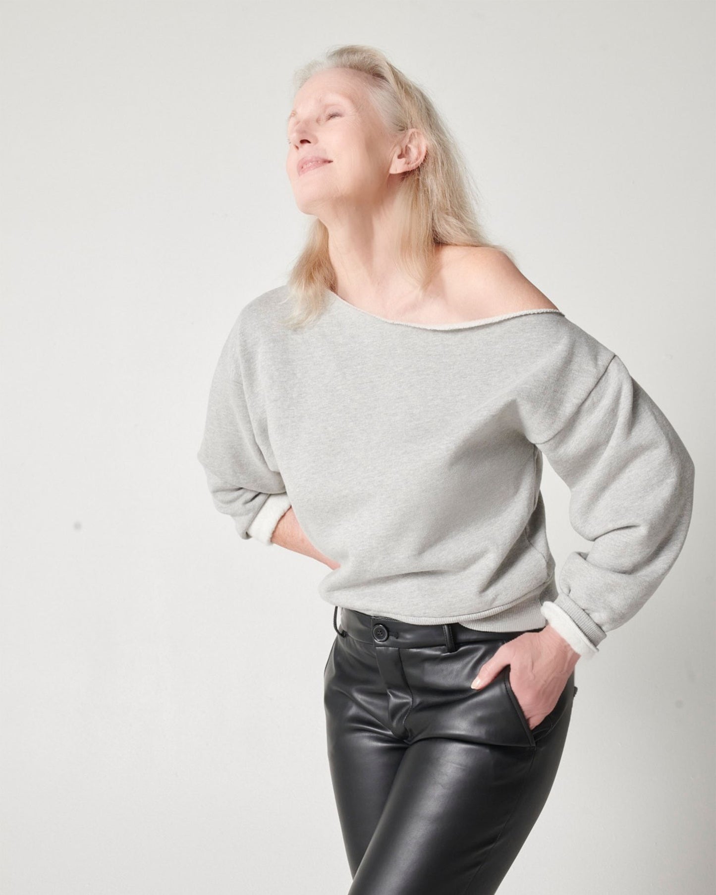 Heather grey cotton fleece off-the-shoulder sweatshirt on older model in black leather pants while looking up