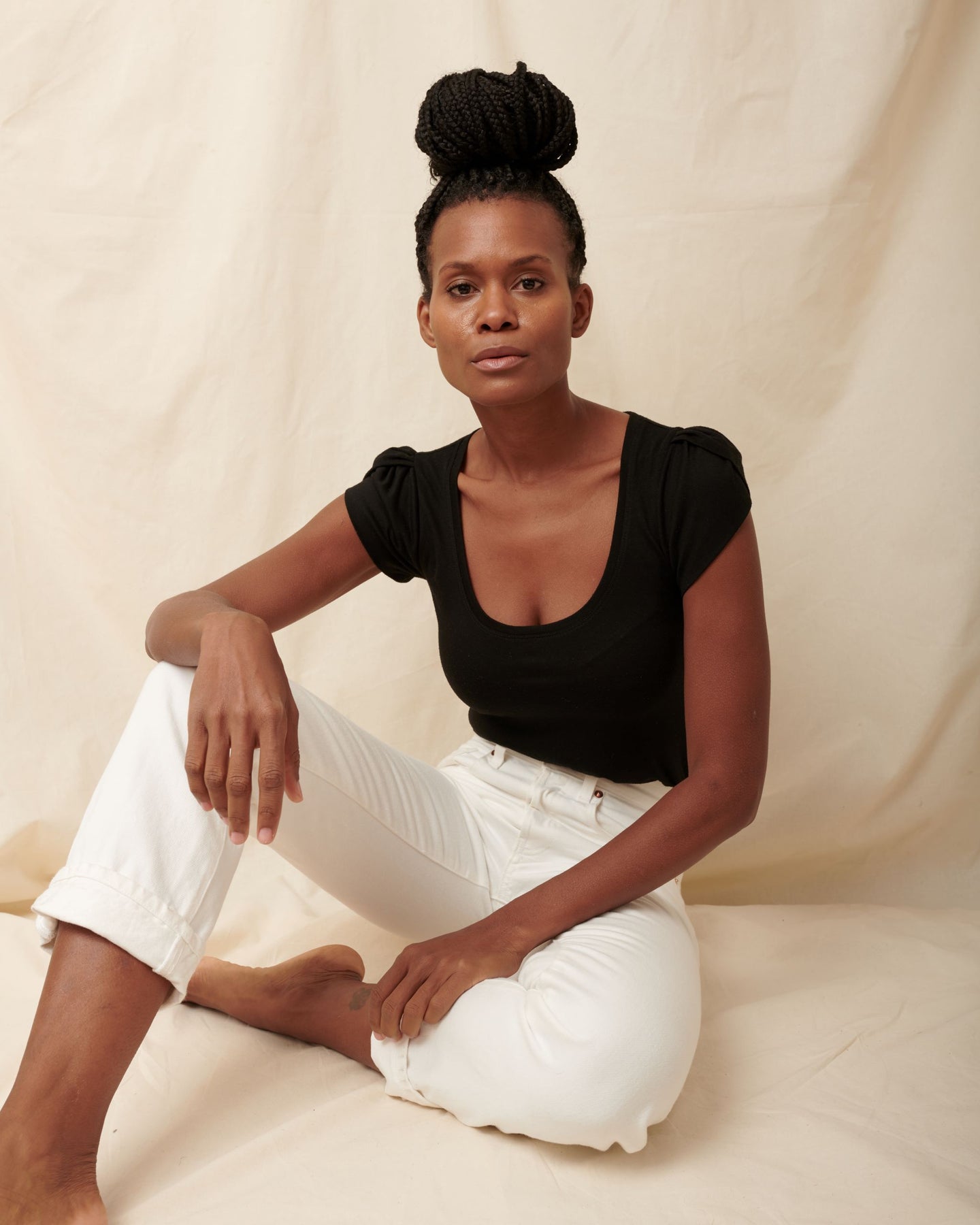 Black supima cotton tulip sleeve scoopneck tee on model sitting on floor wearing white jeans