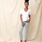 Black model wearing white organic cotton v-neck sweatshirt and blue jeans with hand in pocket and bun in hair