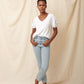Black model wearing white organic cotton v-neck sweatshirt and blue jeans with hands in front pockets and bun in hair