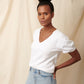 Black model wearing white organic cotton v-neck sweatshirt and blue jeans with hands in back pockets and bun in hair