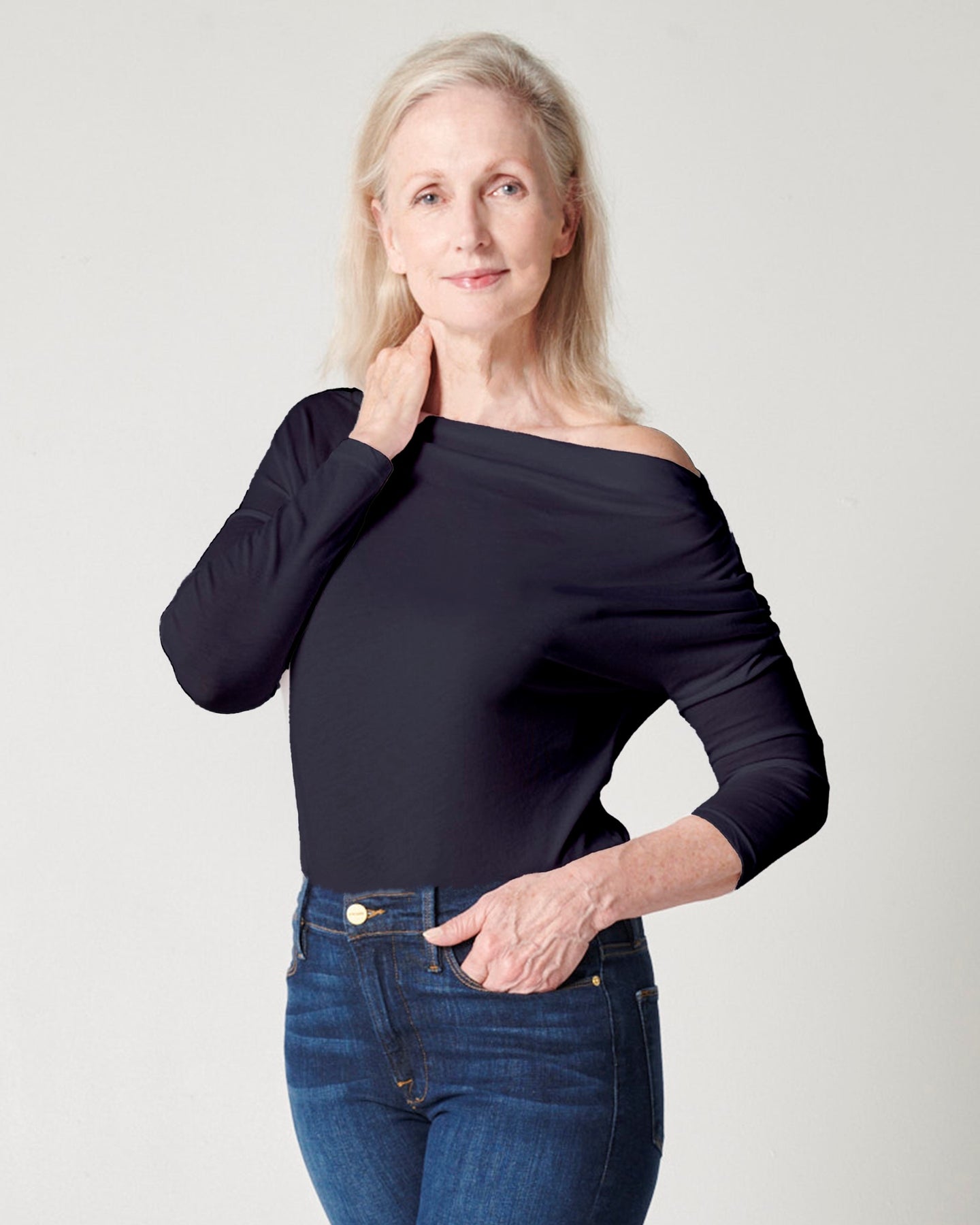 Dark navy supima cotton off-the-shoulder tshirt on older, white model with hand on neck and other in pocket wearing blue jeans