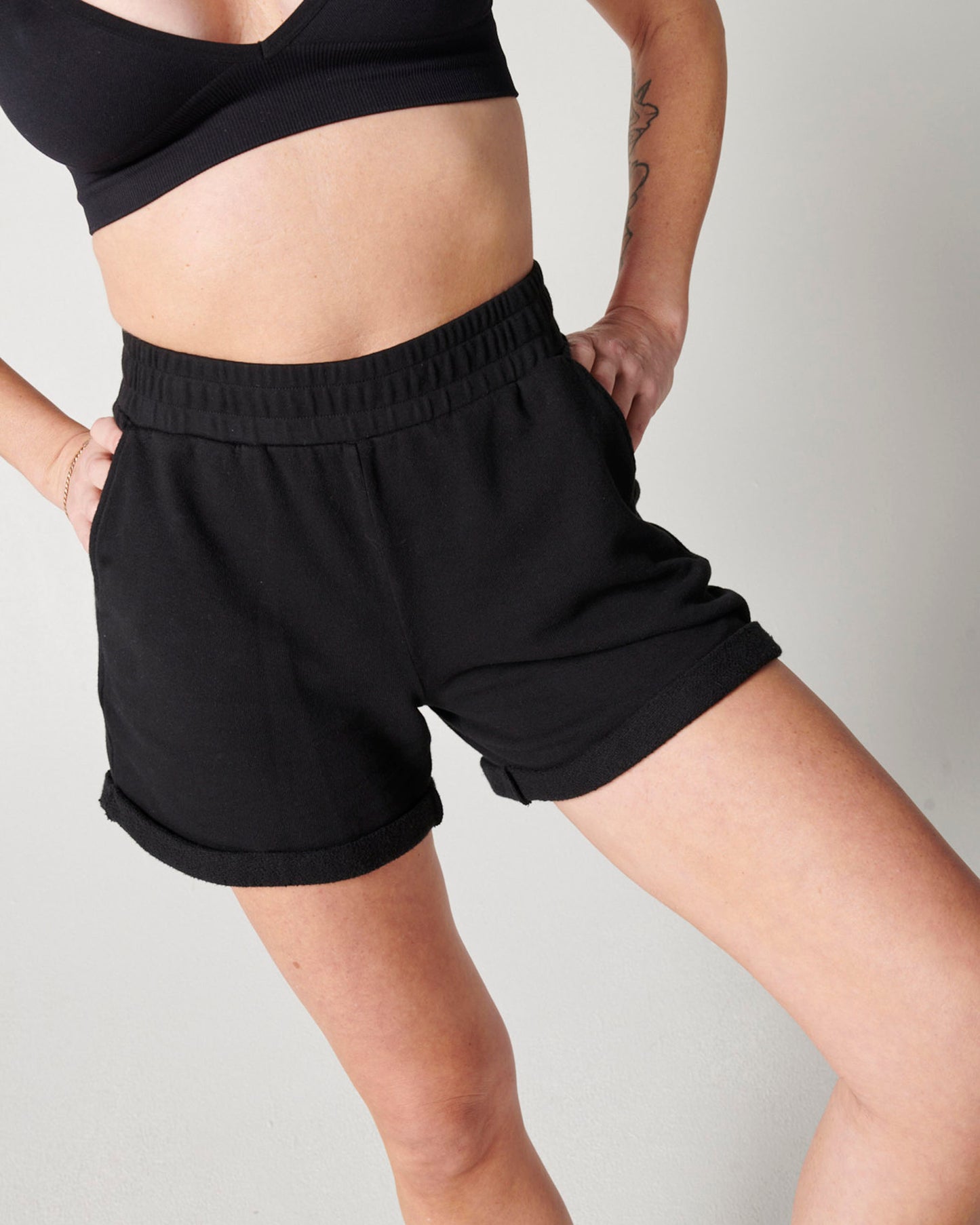 Black organic cotton sweat shorts and black bra on woman's body with hands on hips