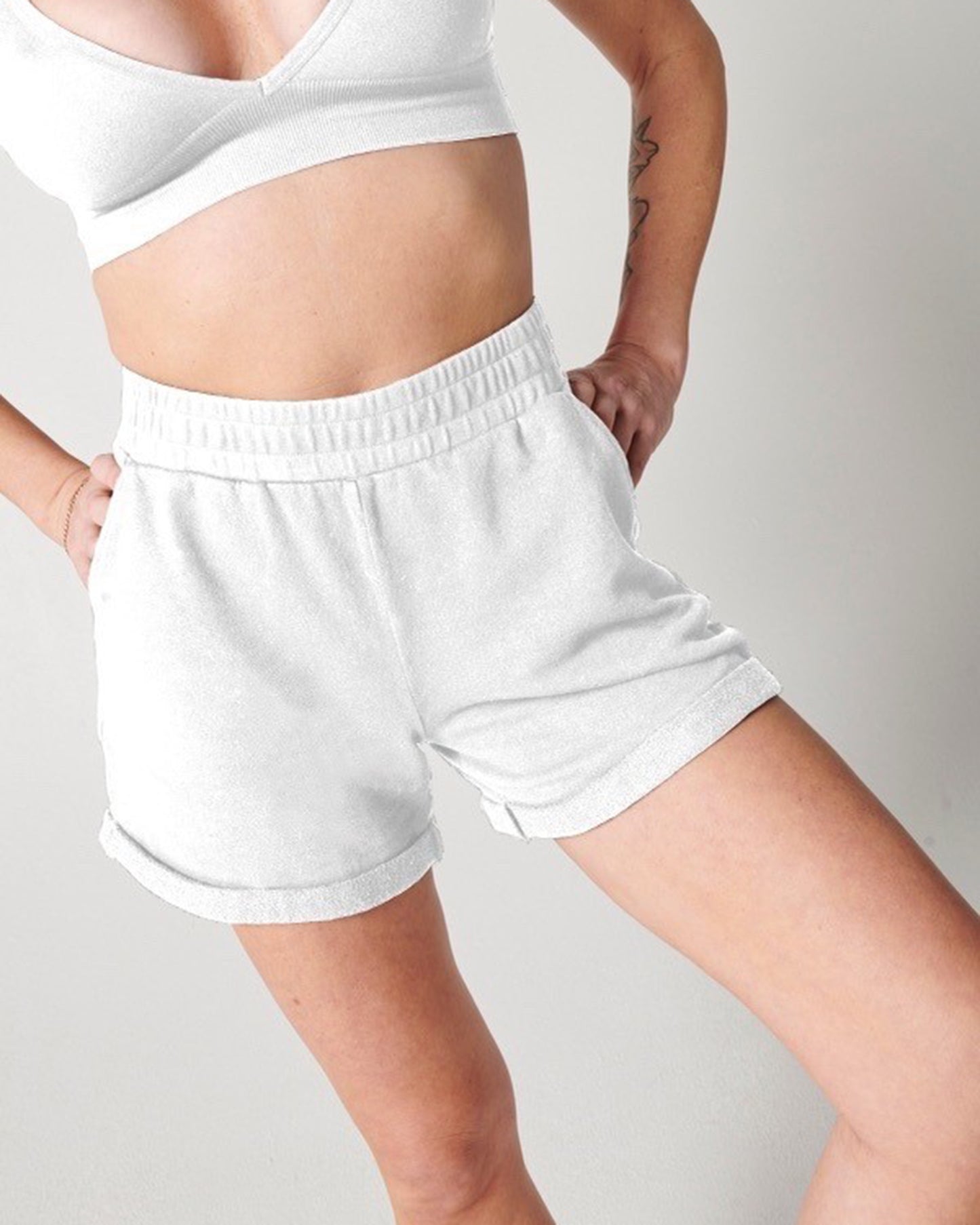 White organic cotton sweat shorts and white bra on woman's body with hands on hips
