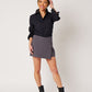 Black cotton long sleeve classic button down tucked into grey skort on smiling asian model holding head and wearing black boots