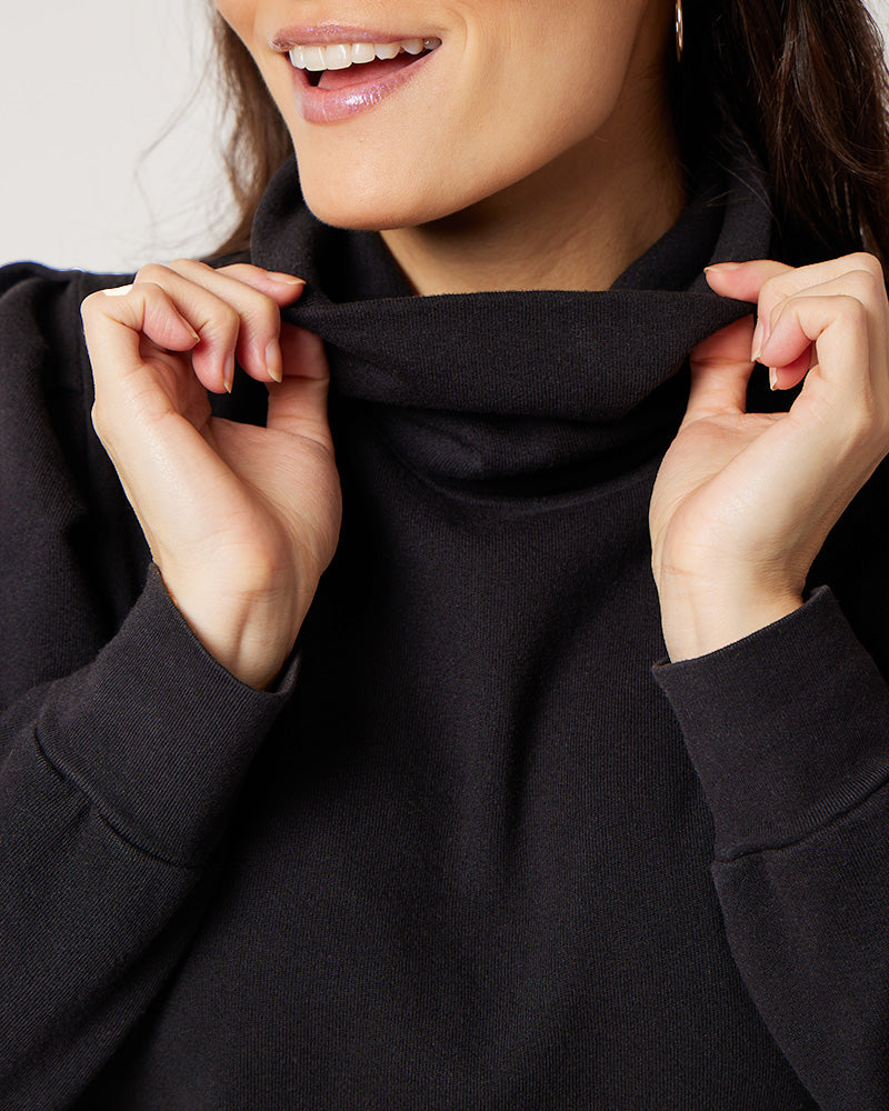 Detail of model holding neck of black organic cotton turtleneck while smiling