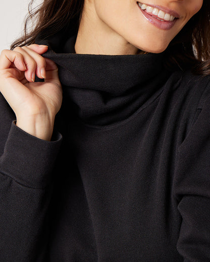 Detail of model holding neck of black organic cotton turtleneck while smiling