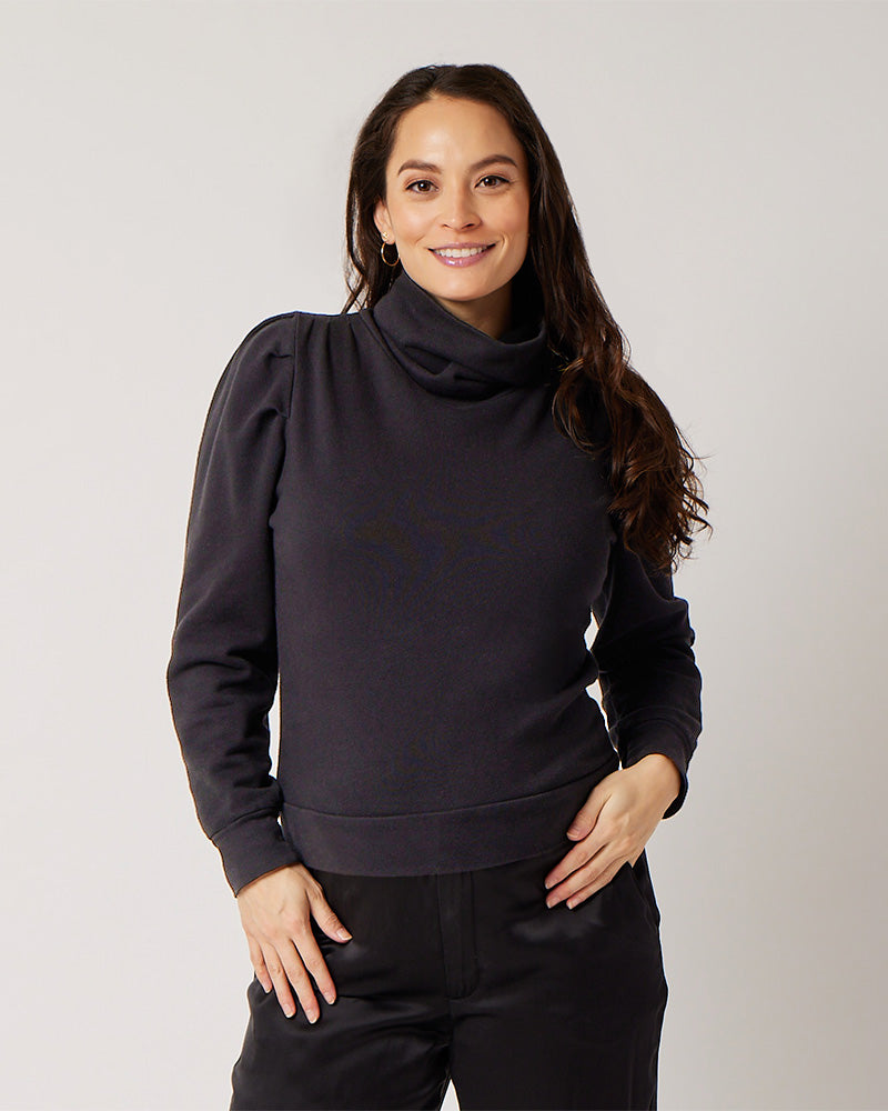 Black organic cotton turtleneck on smiling pregnant model in black silk pants holding belly