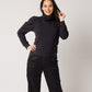 Black organic cotton turtleneck on smiling pregnant model in black silk pants with hand on hip and other holding hair