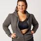 Grey cotton fleece puff sleeve zip up sweatshirt partially zippeed on model wearing black recycled polyester sports bra, black leggings, ponytail and gold hoops with hands on hips