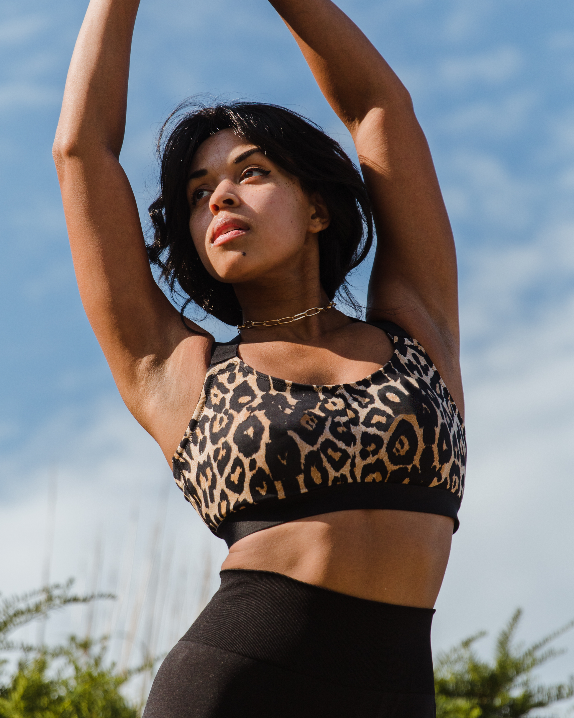 Leopard recycled polyester sports bra on fuller bust model with hands in air