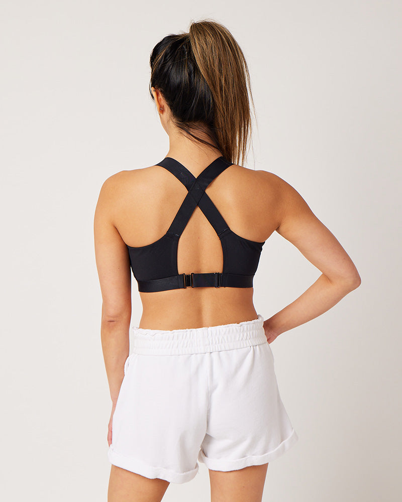 Back detail of black recycled polyester sports bra with magnetic clasp and adjustable slider on model wearing white cotton sweat shorts and ponytail