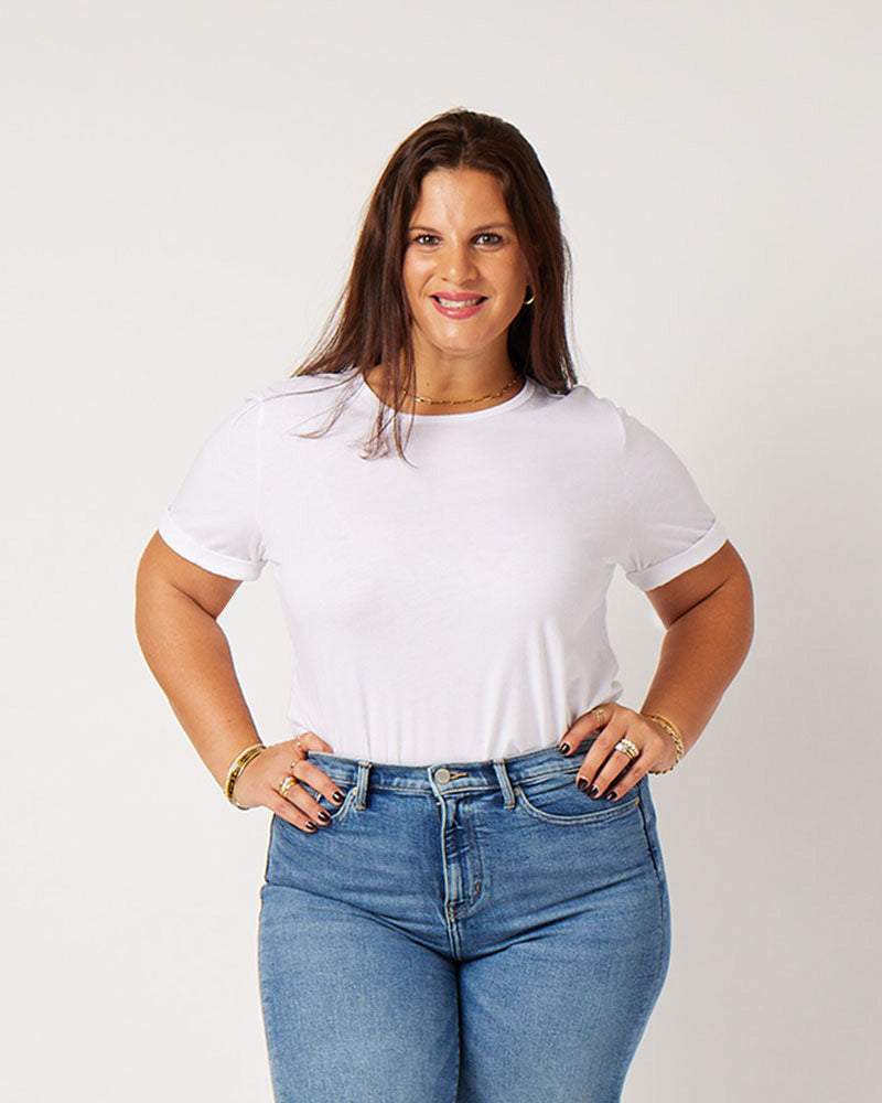 Close-up of white cotton rolled sleeve tshirt on smiling brunette model wearing gold jewelry and blue jeans