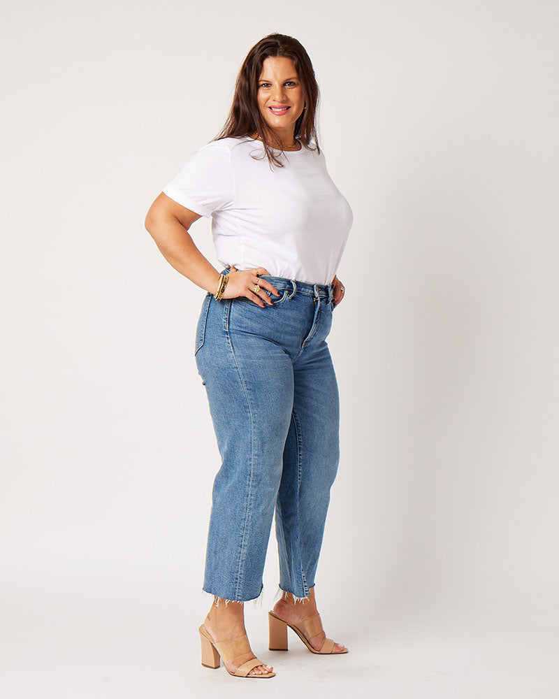 White cotton rolled sleeve tshirt on smiling brunette model wearing gold jewelry, blue jeans and nude heels