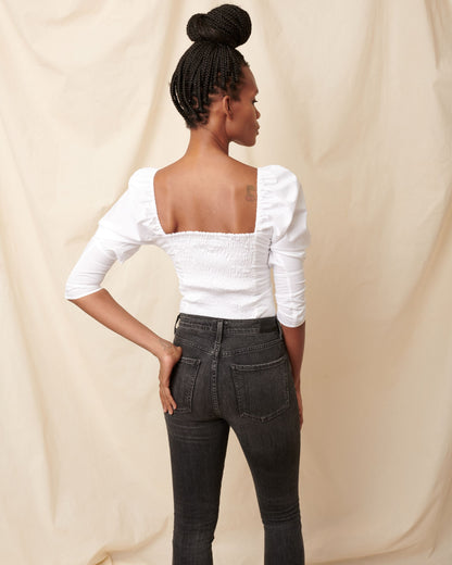 Back of white cotton ruched top on black model wearing black jeans and hair in bun